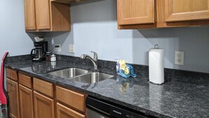 Une cuisine dotée de meubles en bois, d’un plan de travail en granit, d’un évier en acier inoxydable et d’un lave-vaisselle.