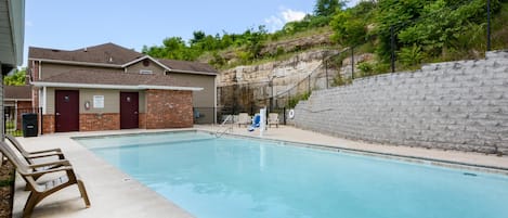 Uma piscina com um edifício de tijolos, um muro de pedra e uma colina gramada ao fundo.