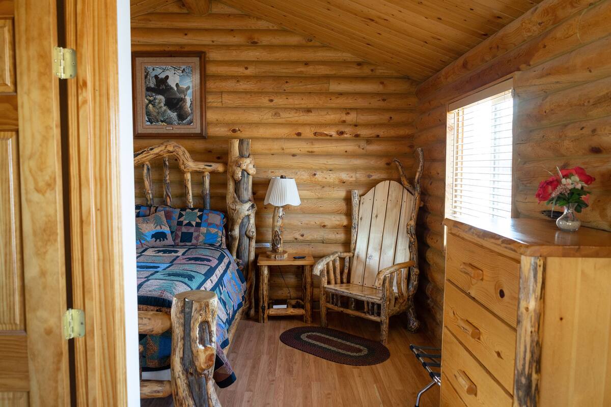 Una habitación tipo cabaña de madera con una cama, un escritorio, una silla y un aparador.