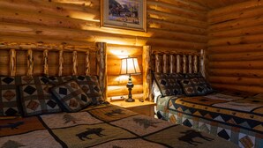 A log cabin room with two beds, a framed picture on the wall, and a lamp on a nightstand.