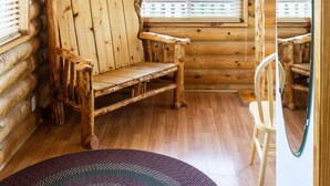A log cabin interior with a wooden bench, a chair, and a window with blinds.