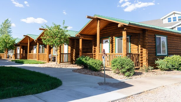 A row of log cabin-style cabins with a green roof, wooden decks, and a clear sky.