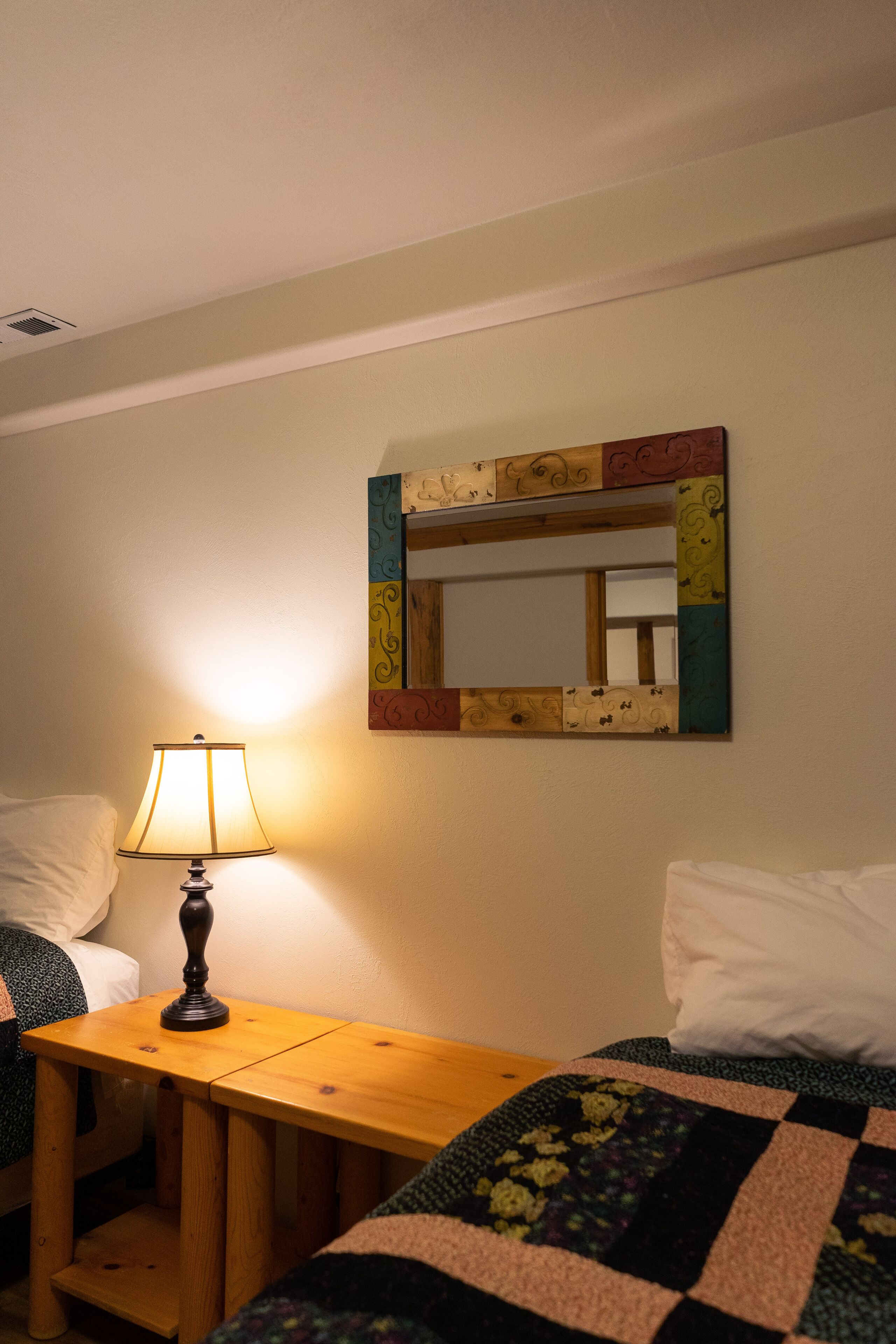 A bedroom with a bed, a bedside table with a lamp, and a mirror on the wall.