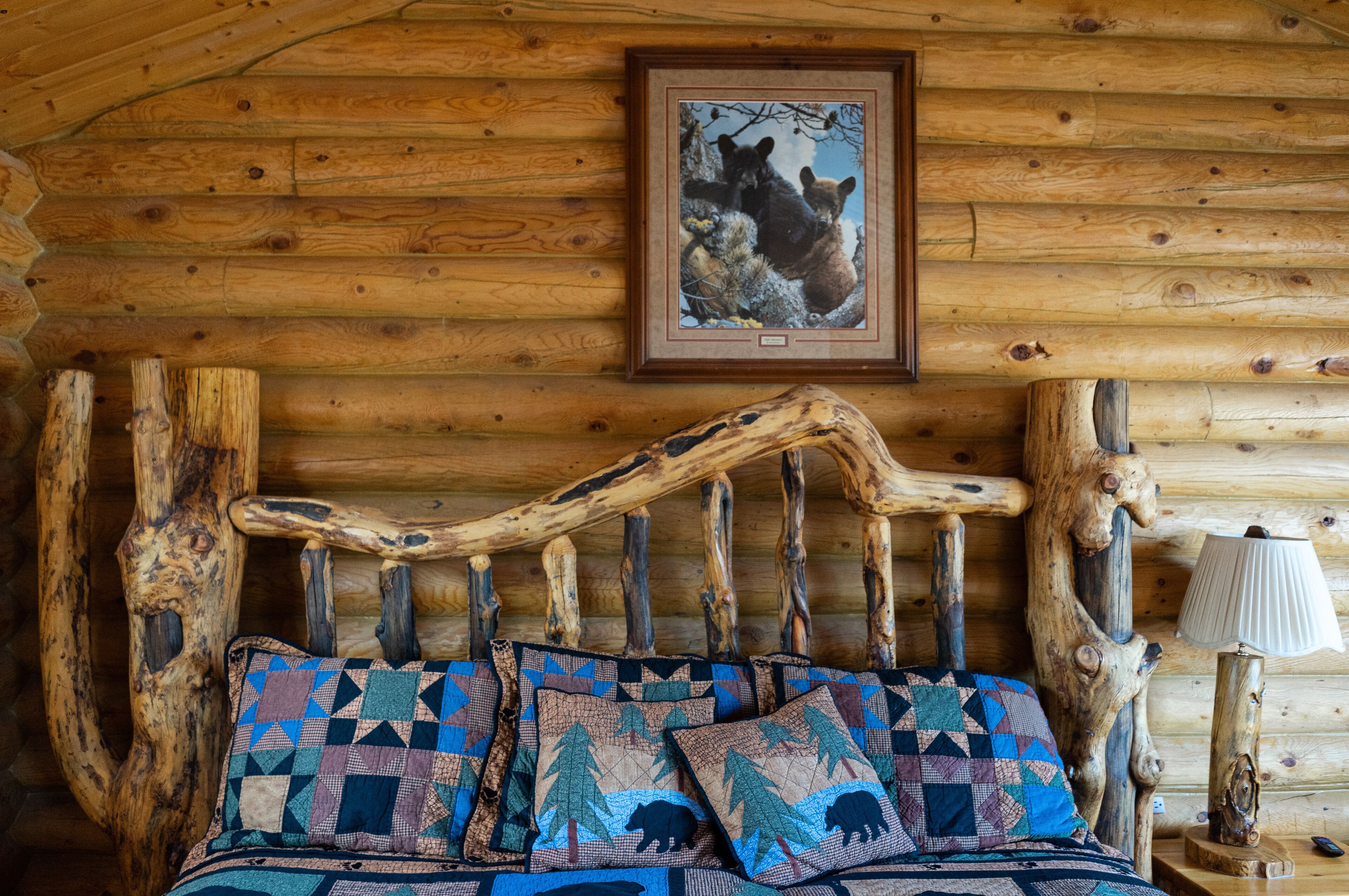 A rustic wooden cabin interior with a log wall, a wooden bed frame, and a framed picture of bears on the wall.