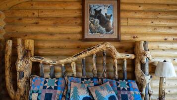 A rustic wooden cabin interior with a log wall, a wooden bed frame, and a framed picture of bears on the wall.
