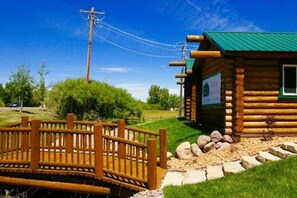A wooden cabin with a green roof, surrounded by a wooden fence and a stone pathway.