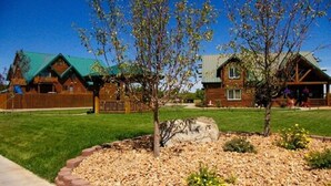 A wooden cabin-style building with a green roof, surrounded by a well-maintained lawn and a rock garden.