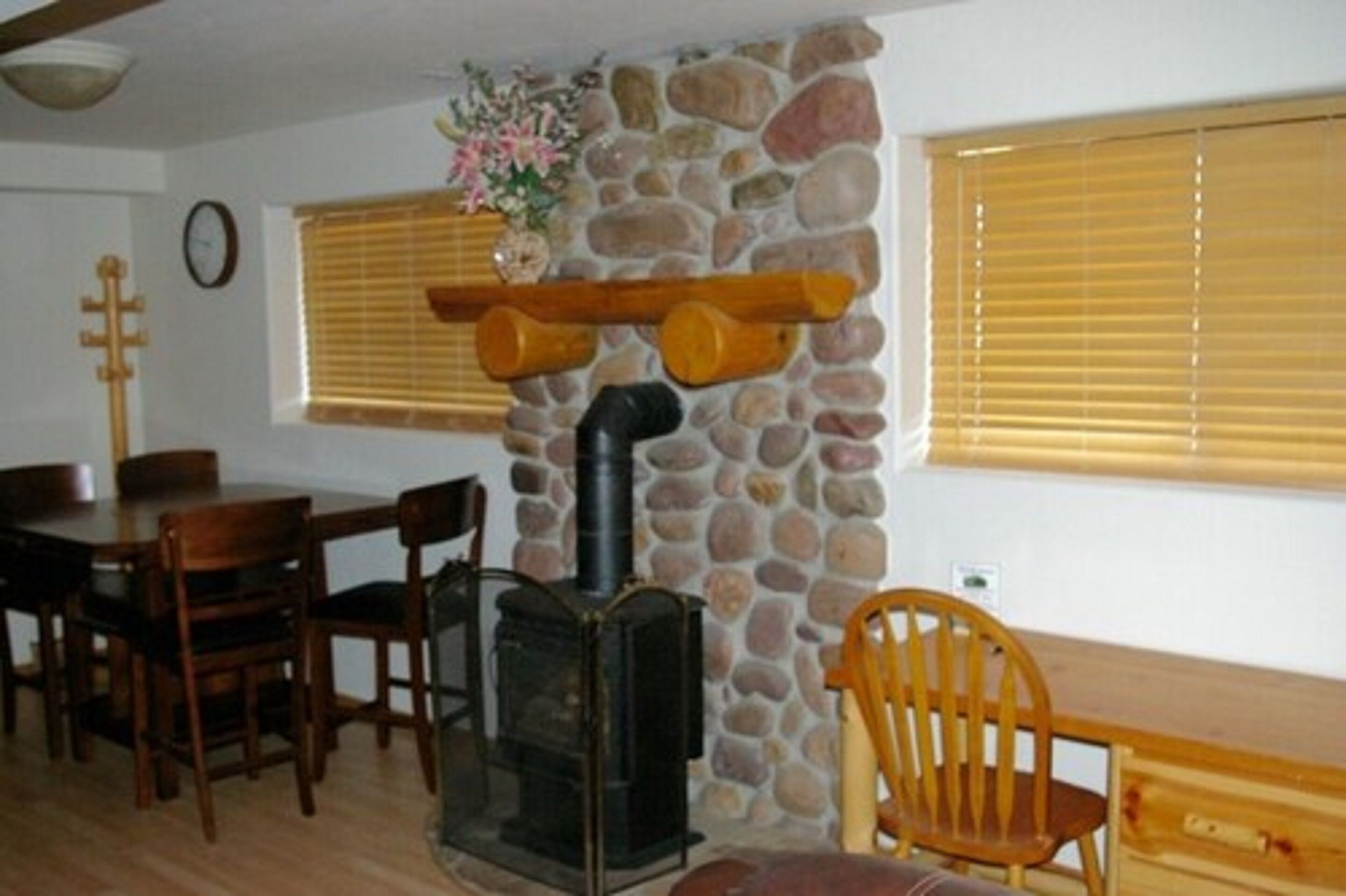Una habitación acogedora con pared de piedra, una mesa de madera, sillas, chimenea y ventana con persianas.