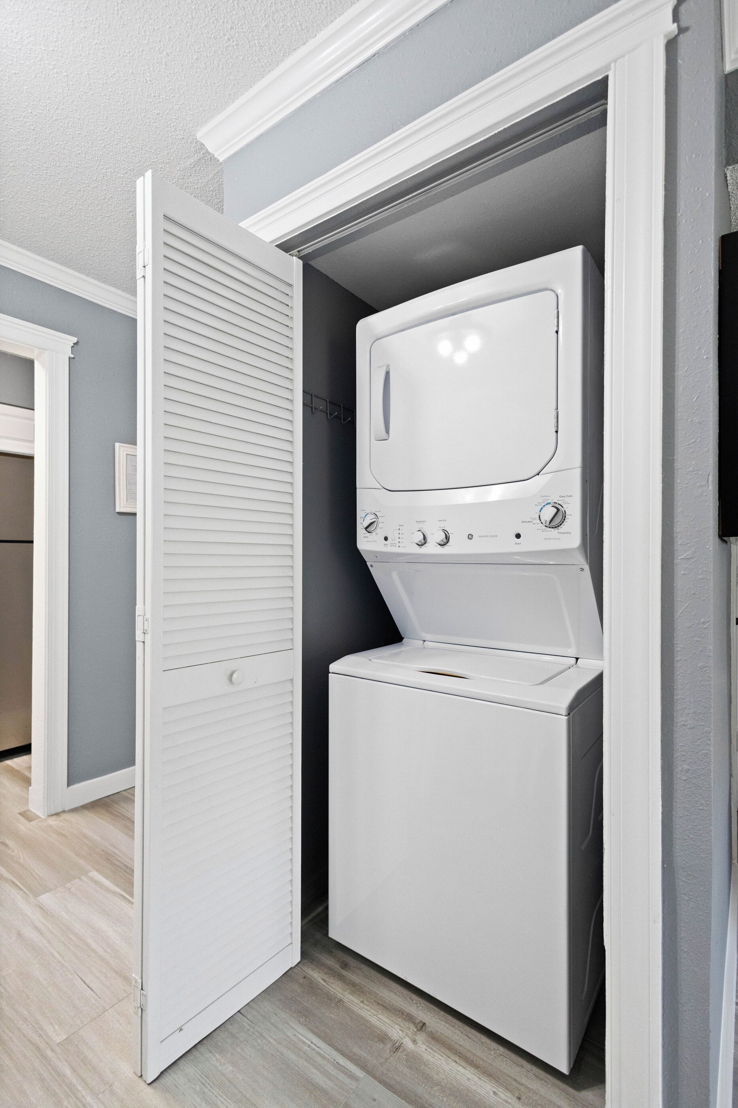 A compact laundry room with a front-loading washer and dryer, a white door, and a light gray wall.