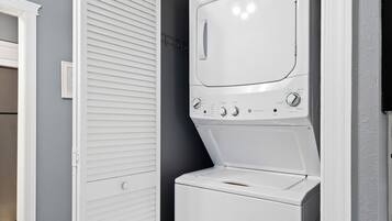 A compact laundry room with a front-loading washer and dryer, a white door, and a light gray wall.