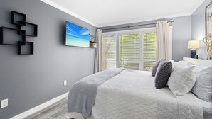 A bedroom with a large bed, a TV on the wall, and a window with blinds.