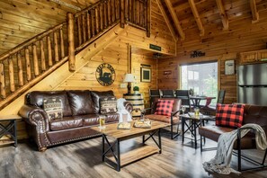A wooden interior with a staircase, leather sofas, a wooden coffee table, and a refrigerator.