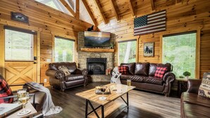 Ein gemütliches Blockhaus-Interieur mit Kamin, Ledersofas, Fernseher und Holzwänden.