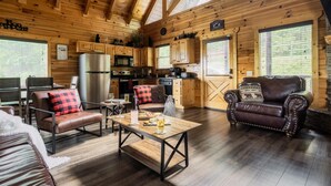 Ein gemütliches Blockhaus-Interieur mit Holzvertäfelung, einer Essecke mit Tisch und Stühlen, einer Küche mit modernen Geräten und einem Kamin.