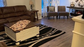 Un salon avec un canapé marron, une commode blanche, un tapis à motifs et un ventilateur de plafond.