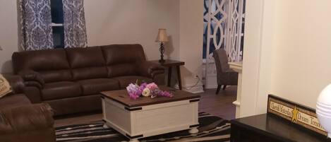 A living room with a brown sofa, a white coffee table with flowers, a ceiling fan, and a zebra-patterned rug.