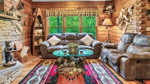 L'intérieur chaleureux d'un chalet avec un canapé en cuir, une table basse en verre et une décoration rustique comprenant une statue d'ours et un crâne de vache.