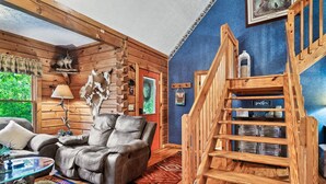 L’intérieur chaleureux d’un chalet avec un fauteuil inclinable en cuir, un escalier en bois et une décoration rustique comprenant une étagère murale et un objet décoratif suspendu.