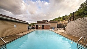 Una piscina rectangular con un cartel de prohibición de saltos, rodeada de edificios y un muro de piedra.