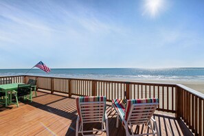 Una terraza de madera con una mesa y sillas, con vista a una playa y al océano, y una bandera.