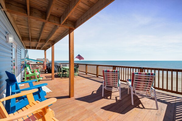 Una terraza de madera con mobiliario exterior, vista al océano y una bandera estadounidense.