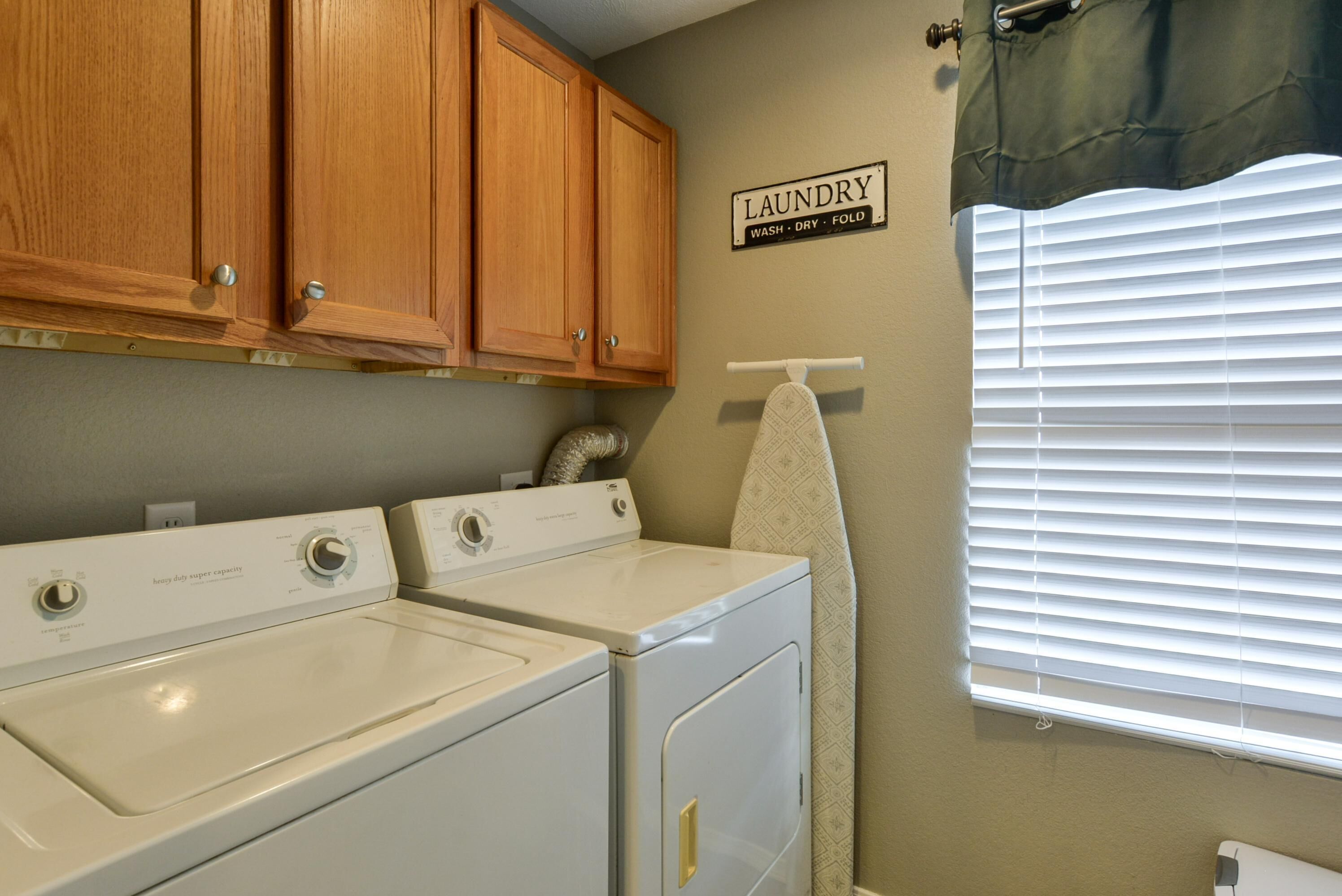 A laundry area with wooden cabinets, a wall-mounted sign, and a window with blinds.