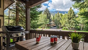 A wooden deck with a grill and canned beverages, overlooking a mountainous landscape.
