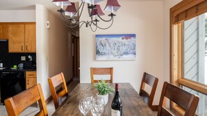 A dining table with chairs, a bottle of wine, and wine glasses. There is a potted plant on the table.