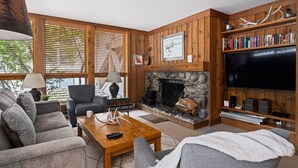 A cozy living room with a fireplace, wooden walls, and a bookshelf.