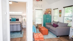 A room with a bed, a grey sofa, orange ottomans, and a teal cabinet.