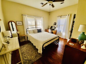 Une chambre à coucher avec un lit, un bureau, une chaise, un miroir et une fenêtre avec des rideaux.
