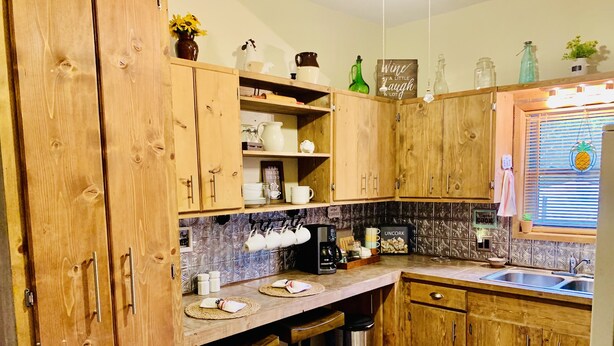 A kitchen with wooden cabinets, a coffee station, and a window with blinds. - Cozy, Country Cottage close to Oaklawn, near Bypass (Hot Springs)