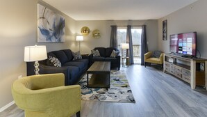 A modern living room with a sofa set, a coffee table, a yellow armchair, a TV, and a large abstract painting on the wall. - GoodVibes Hillside (Branson)