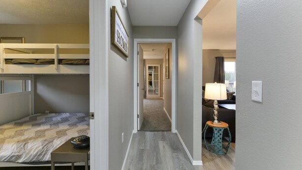 A room with bunk beds, a desk, a lamp, and a hallway leading to another room. - GoodVibes Hillside (Branson)