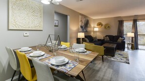 A dining area with a wooden table set for four, a sofa, and a lamp. - GoodVibes Hillside (Branson)