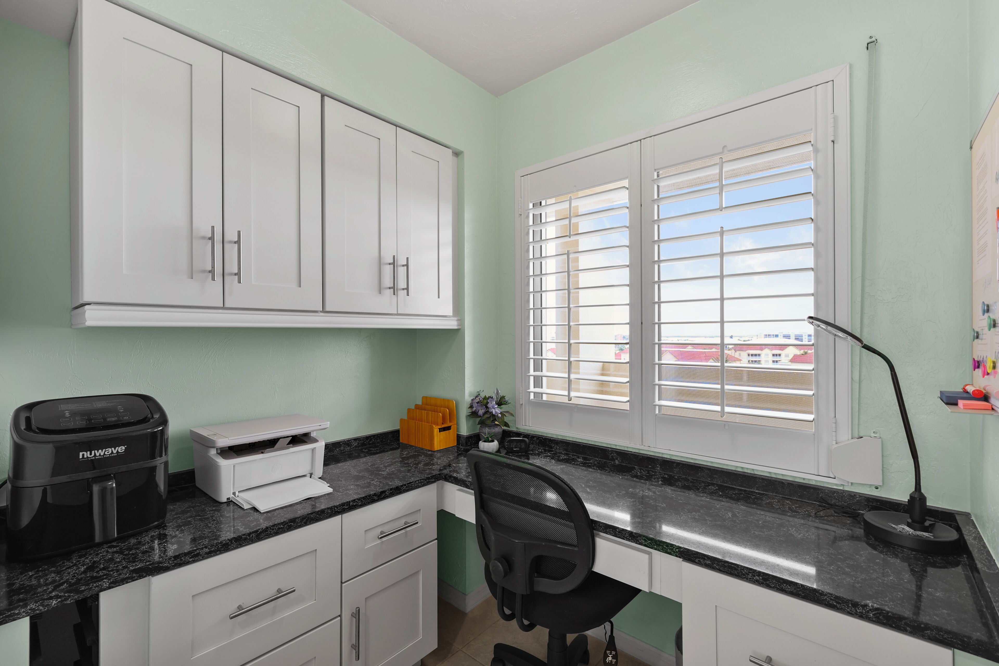 A kitchen with white cabinets, a black countertop, a coffee maker, a printer, and a window with blinds.