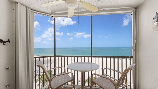 A balcony with a table and chairs, a ceiling fan, and a view of the beach and ocean. - Gulf Coast / Direct Beachfront View - Steps to Sand & Sunset (Fort Myers Beach)