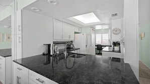 A modern kitchen with white cabinets, a black countertop, and a skylight. - Gulf Coast / Direct Beachfront View - Steps to Sand & Sunset (Fort Myers Beach)
