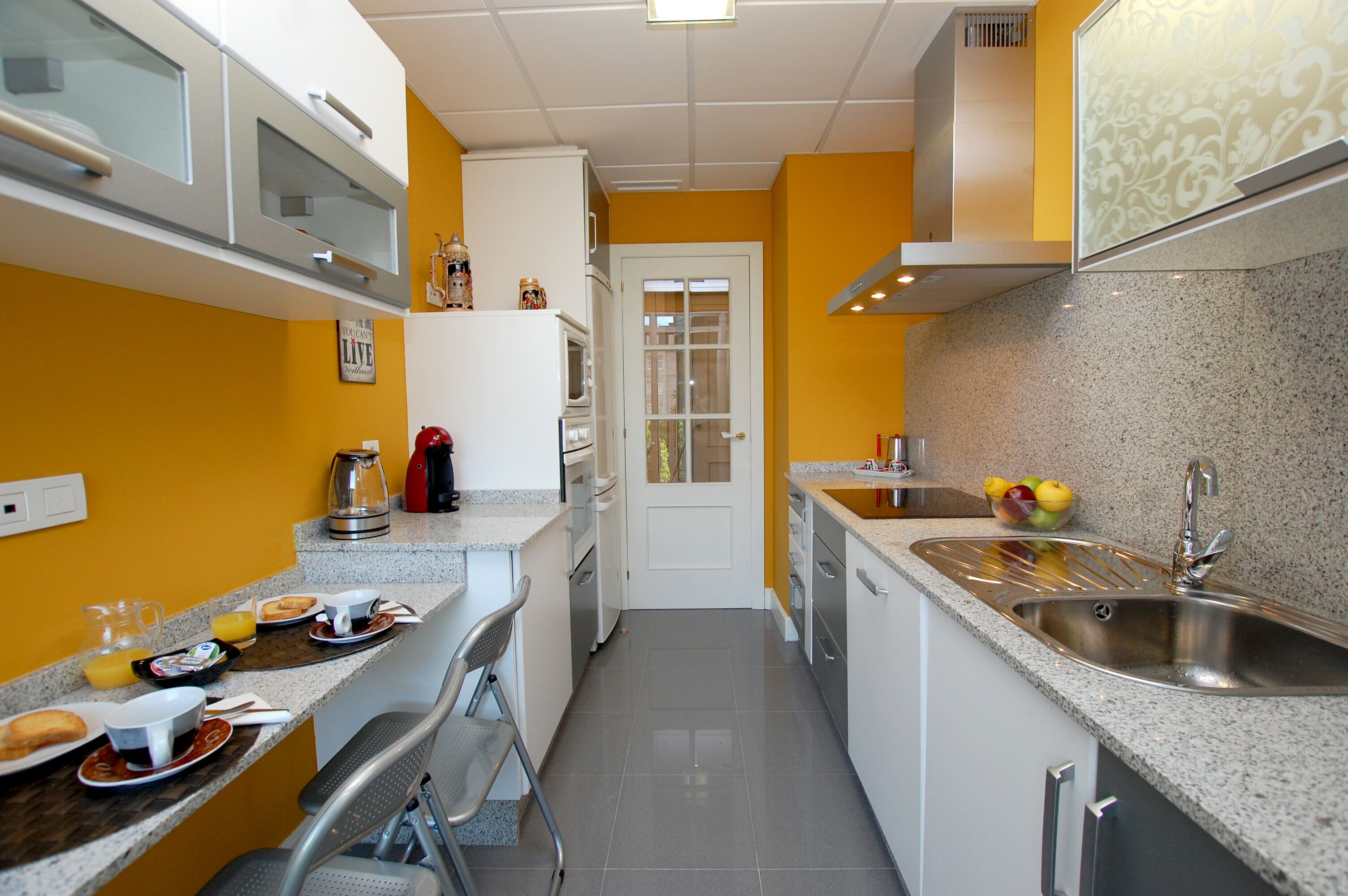 A compact kitchen with white cabinets, a granite countertop, and a stainless steel sink.