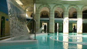 An indoor swimming pool with a water feature, arched ceilings, and a central column.