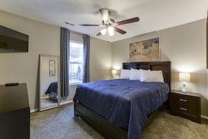 A bedroom with a bed, bedside lamps, a ceiling fan, a TV, and a window with curtains. - Whimsy Vibes (Branson)