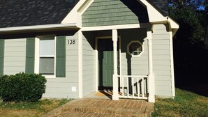 A single-story house with a gabled roof, a front porch with a white railing, and a small circular window above the door. - Upscale And Urban In The City (Columbia)