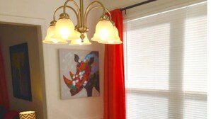A dining area with a round wooden table, red and blue chairs, a chandelier, a painting, and a window with blinds. - Upscale And Urban In The City (Columbia)