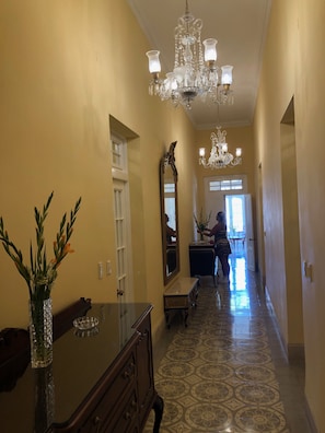 A hallway with a chandelier, a mirror, a vase with flowers, and a patterned floor. - Villa Avana (Havana)
