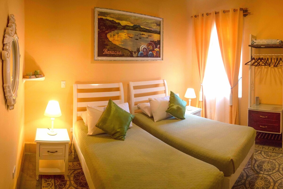 A hotel room with two beds, a painting, a mirror, a desk with a lamp, and a wardrobe.