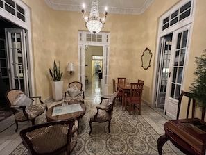 A spacious room with a chandelier, a dining area with wooden chairs and a table, and a large potted plant. - Villa Avana (Havana)