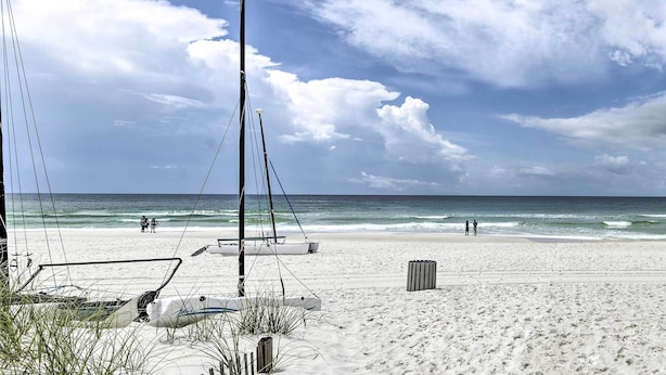 Une plage avec un voilier, un lampadaire et une poubelle.