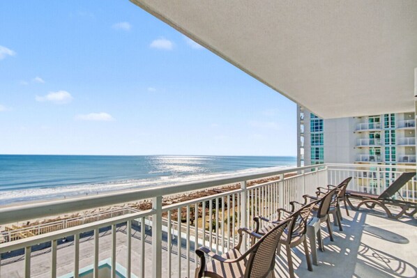 A balcony with a view of the ocean, outdoor furniture, and a building with balconies in the background.