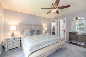 A bedroom with a large bed, two bedside tables with lamps, a ceiling fan, a dresser, and a mirror. - Lake Gaston Lyons creek 3 bedroom plus bunkbed loft 2 bathroom sleeps 10-12 (Macon)