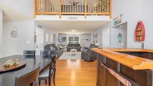 Ein geräumiges Wohnzimmer mit hoher Decke, einem Holzbalkon und einem Essbereich mit Holztisch und -stühlen.